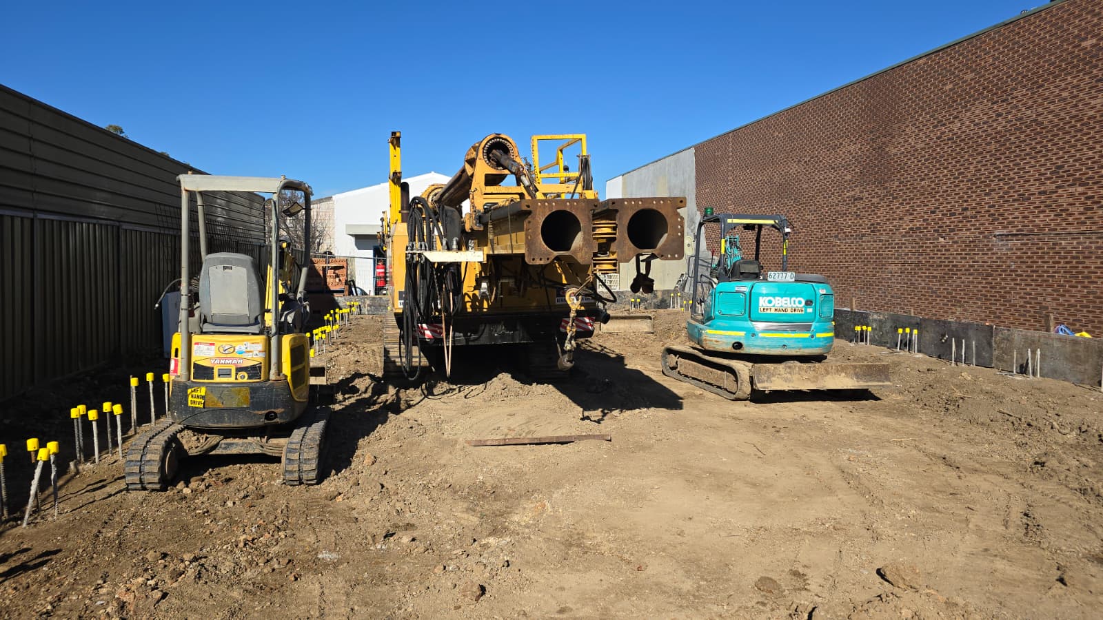 A construction site with a large piling rig and two mini excavators.